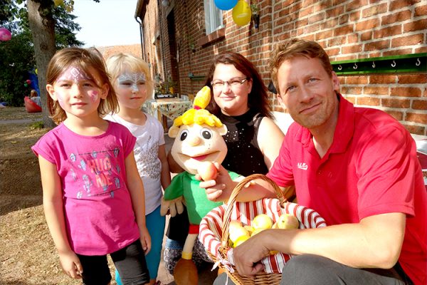 Marko Witte, Kundenbetreuuer bei ALEXMENÜ und das Maskottchen Hopsi freuen sich die Kinder und Eltern persönlich kennenzulernen