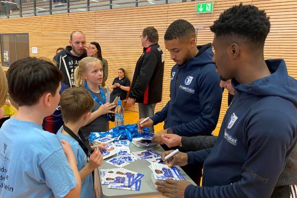 Die Spieler Manfred Osei Kwadwo und Leon Bell Bell des 1. FCM verteilen personalisierte Autogrammkarten. ©Stefanie Böttcher